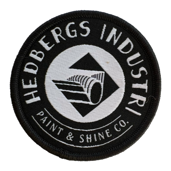 Patch med vår snygga logo Hedbergs Industri AB – Paint & Shine Co. Vävt tygmärke i svart med silvertråd. Framsida.